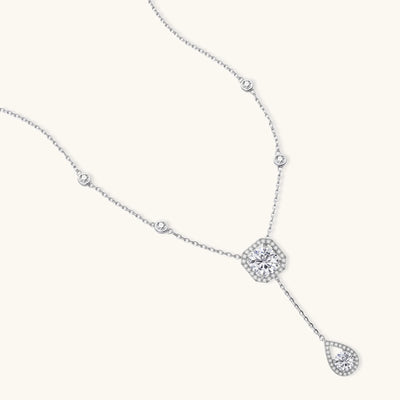 Sterling silver necklace with cushion-cut moissanite in halo setting and teardrop pendant, displayed on cream background.