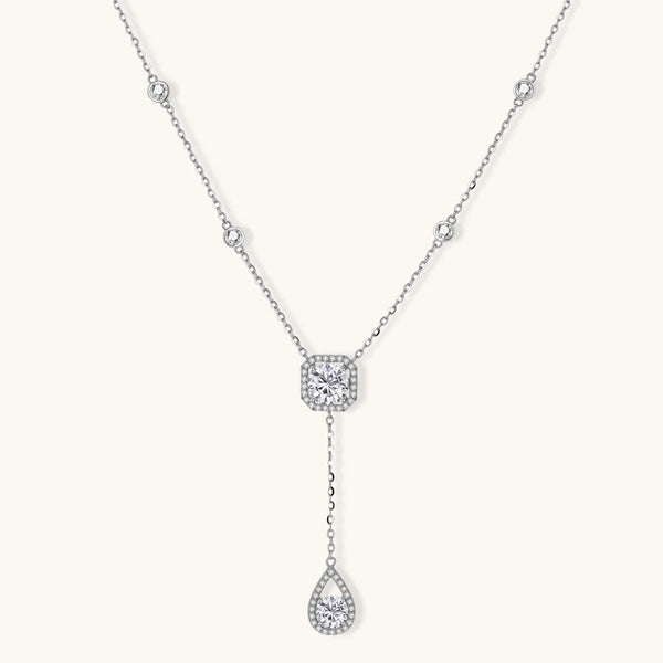 Sterling silver necklace with cushion-cut moissanite in halo setting and teardrop pendant, displayed on cream background.